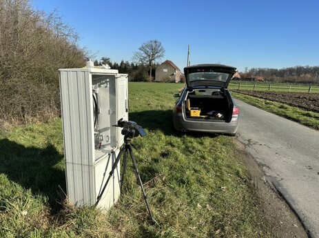 Mein Auto steht am Straßenrand mit offenen Kofferraum damit ich an mein Werkzeug komme. Im Vordergrund ein KVz mit aufgestellten Spleißgerät. 