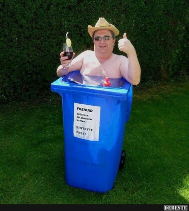 Ein Mann hockt in einer blauen Mülltonne die voll Wasser ist. In der Hand hat er ein Getränk, auf dem Kopf ein Strohhut und er hebt den Daumen um zu zeigen das er zufrieden ist. 